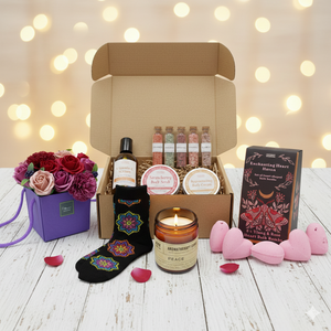 Luxury Valentine's Day spa gift collection featuring a heart-shaped bath bomb set, a purple soap flower bouquet in a gift bag, an amber glass aromatherapy candle, a serenity self-care kit with serum and salts, and floral mandala bamboo socks arranged in a relaxed, romantic setting.